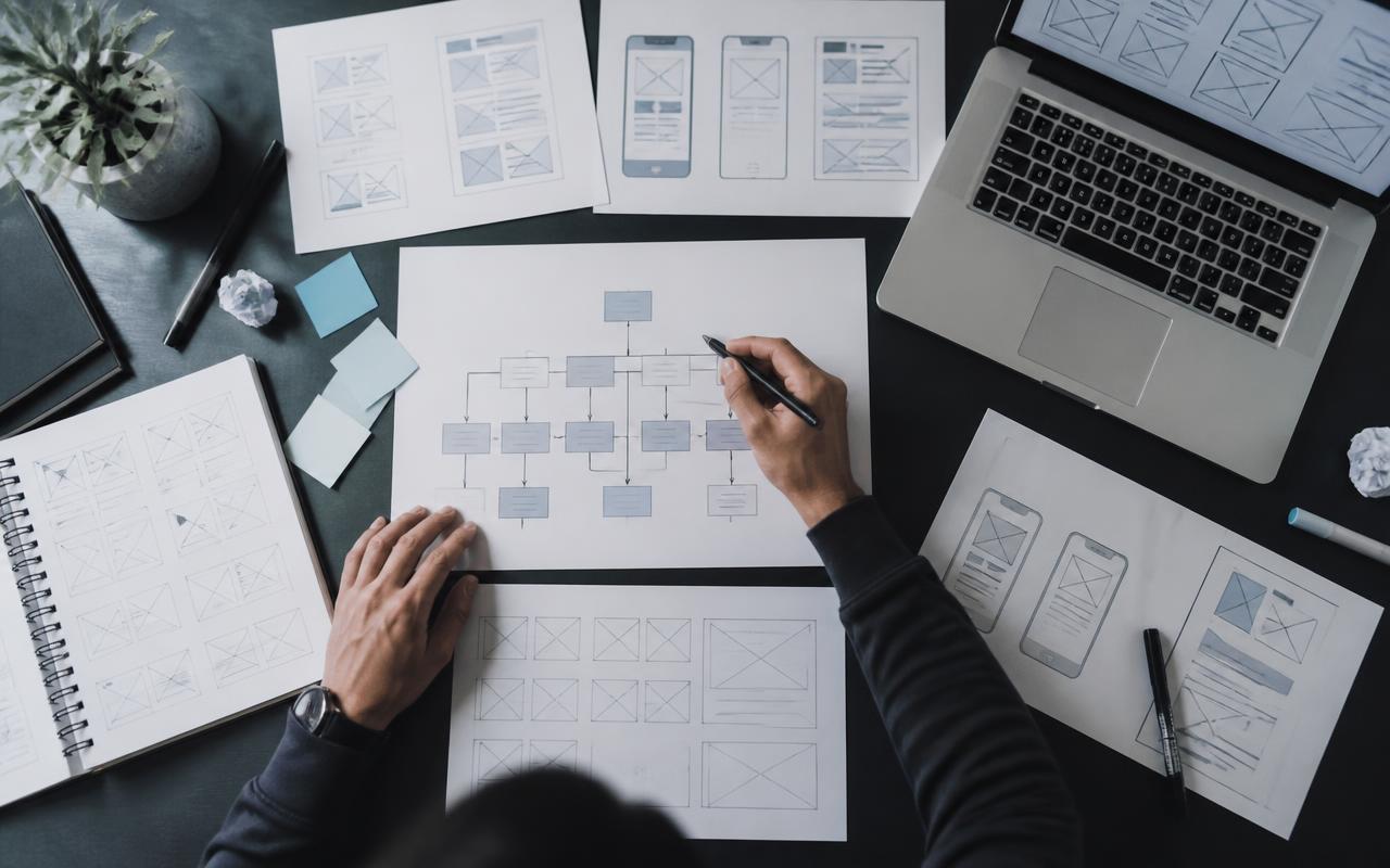 Skizzen von Seitenstruktur und Wireframes auf einem Schreibtisch neben einem Laptop