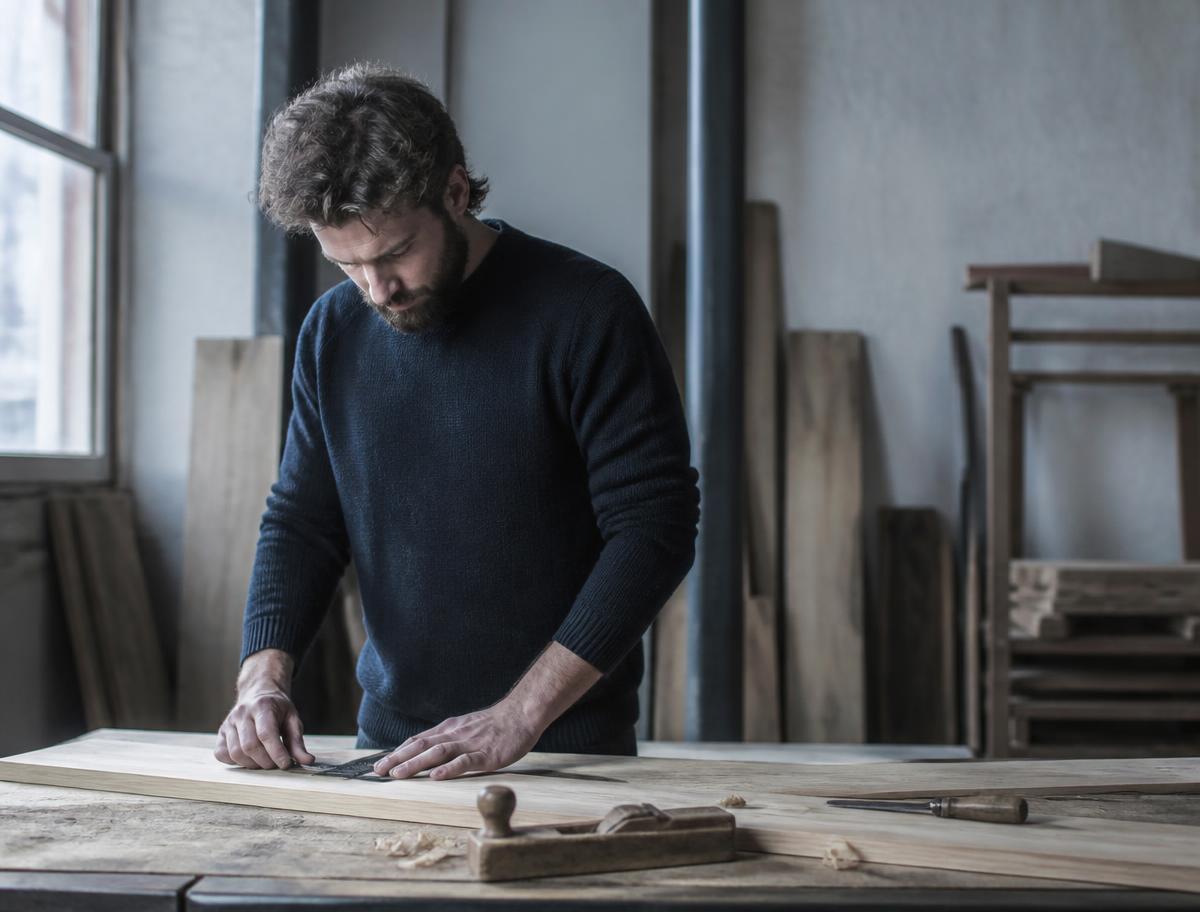 Handwerker misst in seiner Werkstatt ein Holzbrett aus